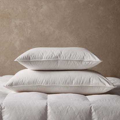 Two white feather and down chamber pillows stacked on a quilt against a limewashed wall